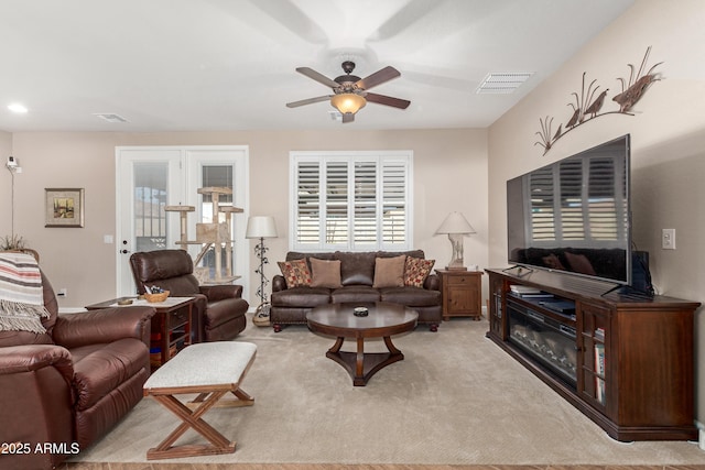 living room with a ceiling fan, visible vents, and light carpet