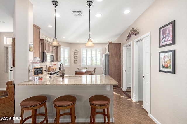 kitchen featuring visible vents, dark wood finished floors, a peninsula, stainless steel appliances, and a sink