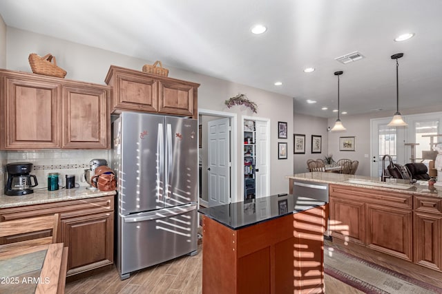 kitchen featuring brown cabinets, visible vents, light wood-style flooring, freestanding refrigerator, and a sink