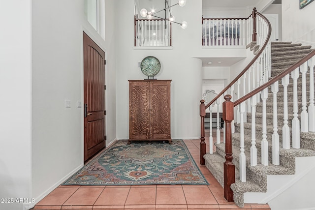 tiled foyer entrance featuring baseboards, a towering ceiling, a chandelier, and stairway