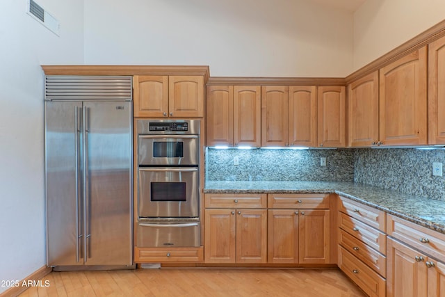 kitchen with a warming drawer, visible vents, light stone counters, stainless steel appliances, and decorative backsplash
