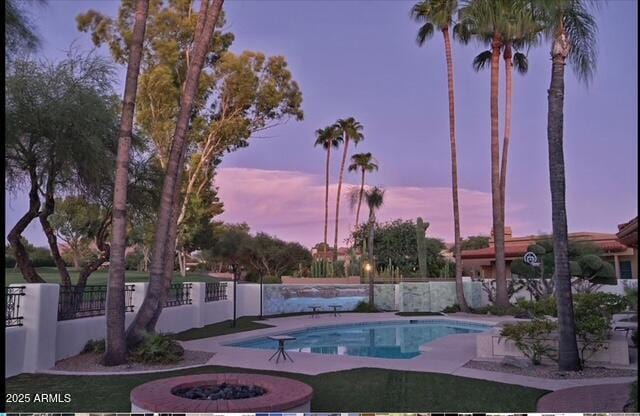 pool at dusk with an outdoor pool and fence