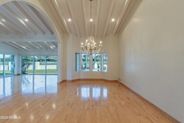 spare room with an inviting chandelier, light wood-style floors, baseboards, and beam ceiling