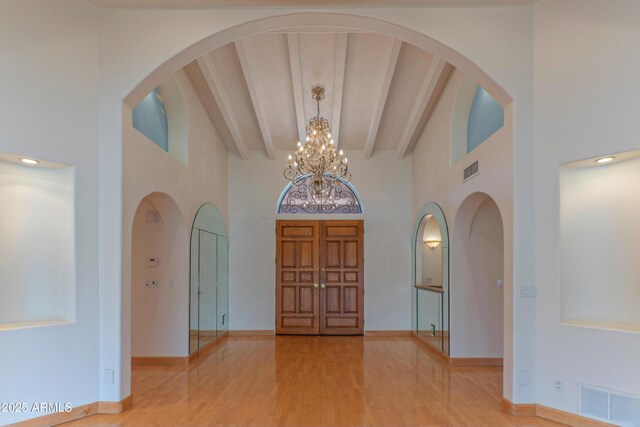 foyer entrance featuring visible vents, beam ceiling, wood finished floors, a towering ceiling, and a chandelier