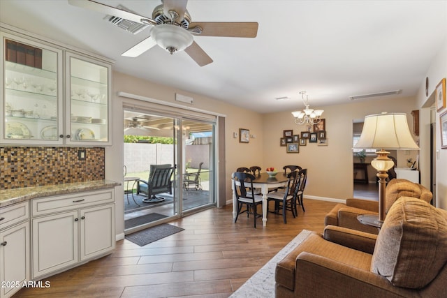 living room featuring visible vents, baseboards, wood finished floors, and ceiling fan with notable chandelier
