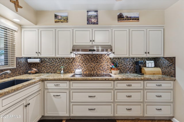 kitchen with black electric stovetop, under cabinet range hood, decorative backsplash, and a sink