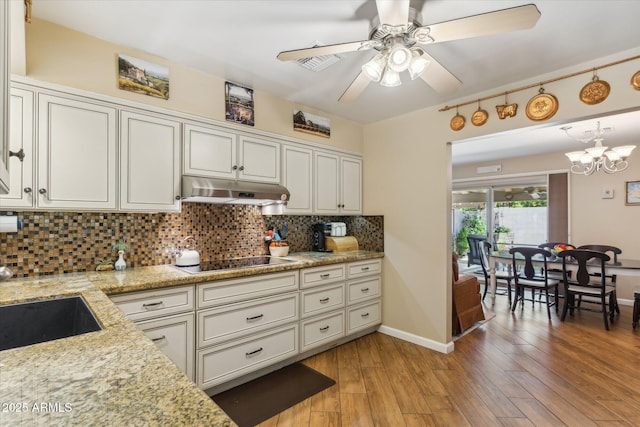 kitchen with tasteful backsplash, baseboards, under cabinet range hood, black electric stovetop, and ceiling fan with notable chandelier