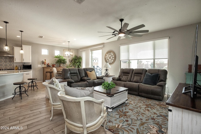 living room with ceiling fan with notable chandelier and light hardwood / wood-style floors