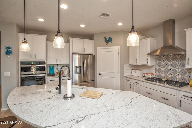 kitchen featuring white cabinetry, an island with sink, wall chimney exhaust hood, and stainless steel appliances