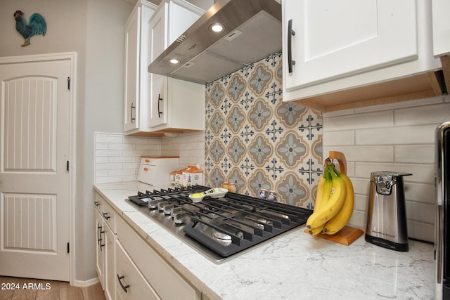 kitchen featuring white cabinetry, wall chimney exhaust hood, backsplash, black gas stovetop, and light wood-type flooring