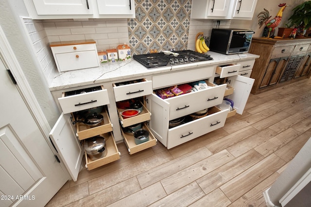 kitchen featuring tasteful backsplash, white cabinetry, light hardwood / wood-style flooring, and stainless steel gas cooktop