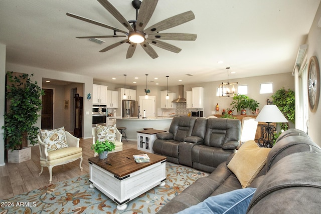 living room with ceiling fan with notable chandelier and light hardwood / wood-style flooring