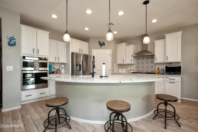 kitchen with pendant lighting, white cabinets, light wood-type flooring, an island with sink, and appliances with stainless steel finishes