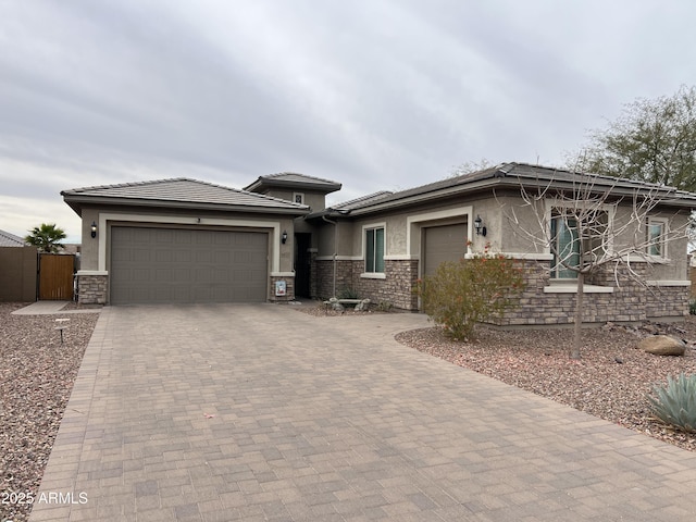 prairie-style house with a garage, stone siding, decorative driveway, and stucco siding