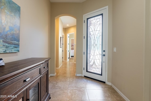 foyer with arched walkways, light tile patterned floors, and baseboards