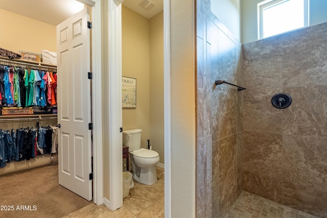 bathroom with visible vents, tiled shower, a walk in closet, and toilet