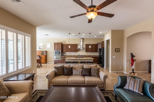 living area with light tile patterned floors, visible vents, arched walkways, baseboards, and ceiling fan