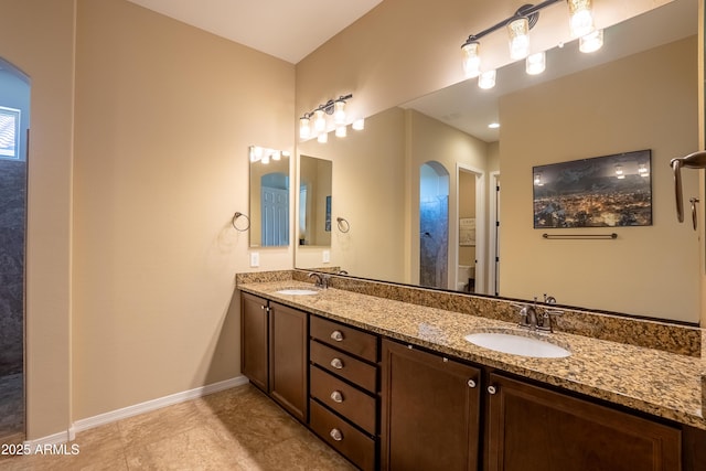 bathroom featuring toilet, a sink, baseboards, and double vanity