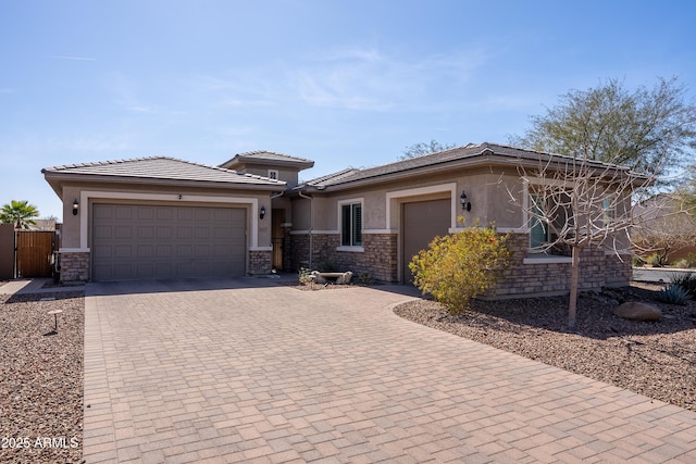 prairie-style house with an attached garage, stone siding, decorative driveway, and stucco siding