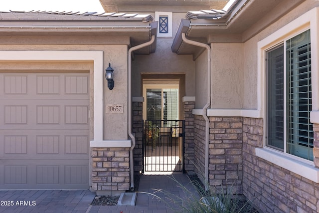 entrance to property with stone siding, an attached garage, and stucco siding