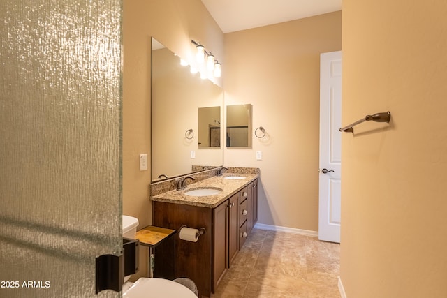 full bathroom featuring double vanity, baseboards, toilet, and a sink