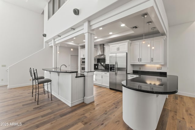 kitchen with stainless steel appliances, wall chimney exhaust hood, dark countertops, and a kitchen breakfast bar