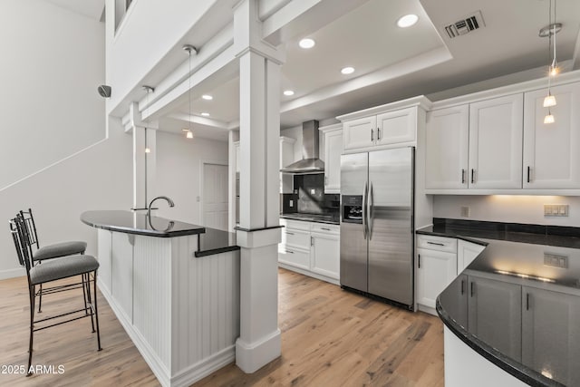 kitchen featuring dark countertops, wall chimney range hood, visible vents, and stainless steel fridge with ice dispenser