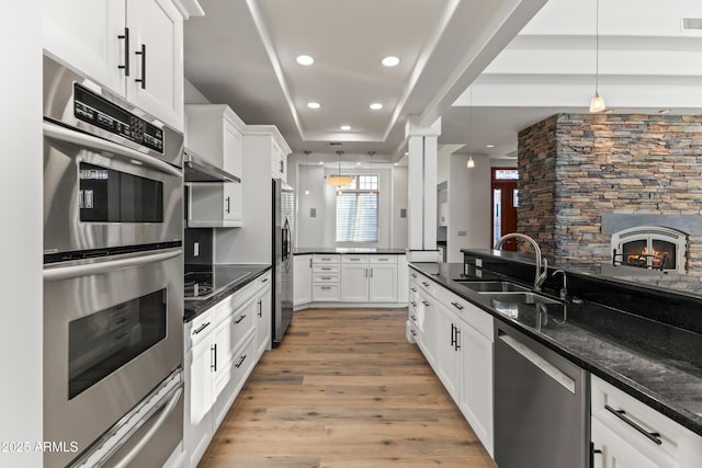 kitchen featuring stainless steel appliances, light wood-style floors, a sink, and hanging light fixtures