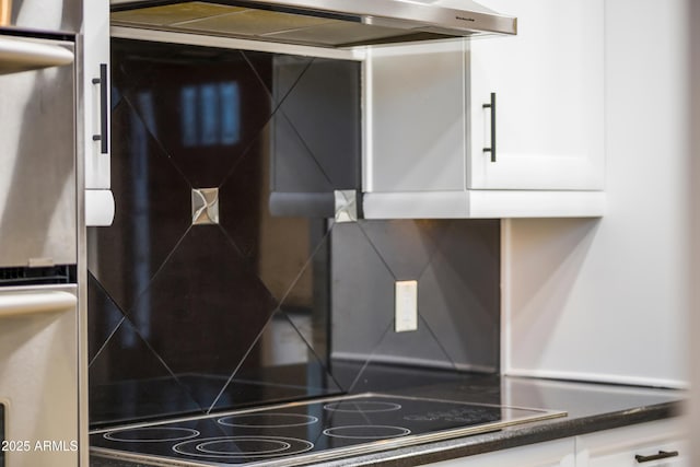 room details with black electric cooktop, under cabinet range hood, white cabinets, tasteful backsplash, and dark countertops