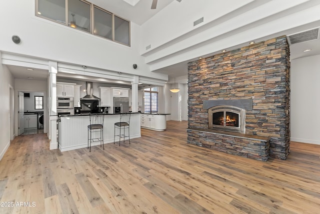 kitchen with visible vents, appliances with stainless steel finishes, open floor plan, washer and dryer, and wall chimney exhaust hood