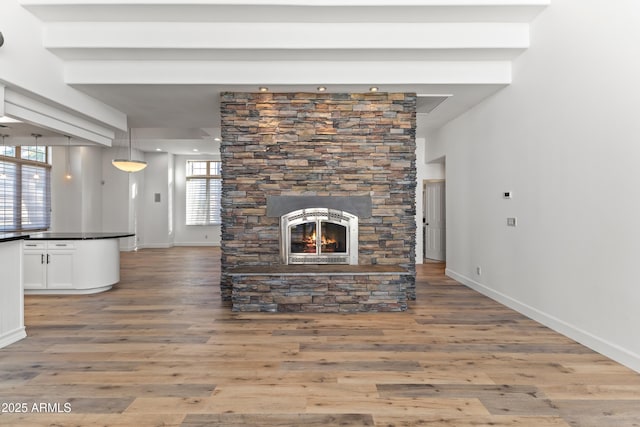 unfurnished living room with a stone fireplace, baseboards, and wood finished floors