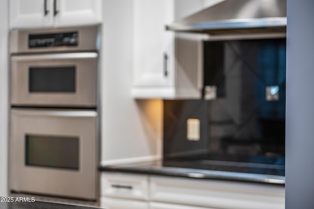 interior details featuring dark countertops, double oven, white cabinets, and exhaust hood