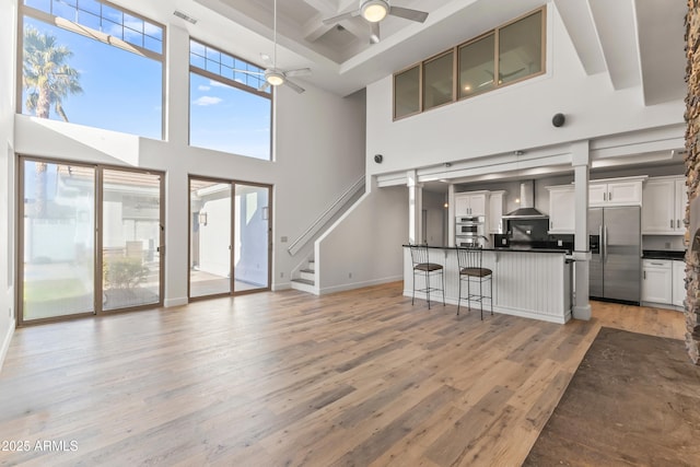 living room featuring baseboards, coffered ceiling, ceiling fan, light wood-style flooring, and beamed ceiling