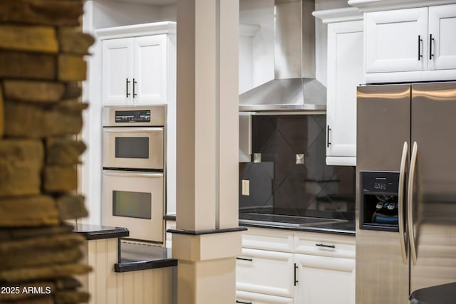 kitchen featuring stainless steel appliances, dark countertops, tasteful backsplash, white cabinets, and wall chimney range hood