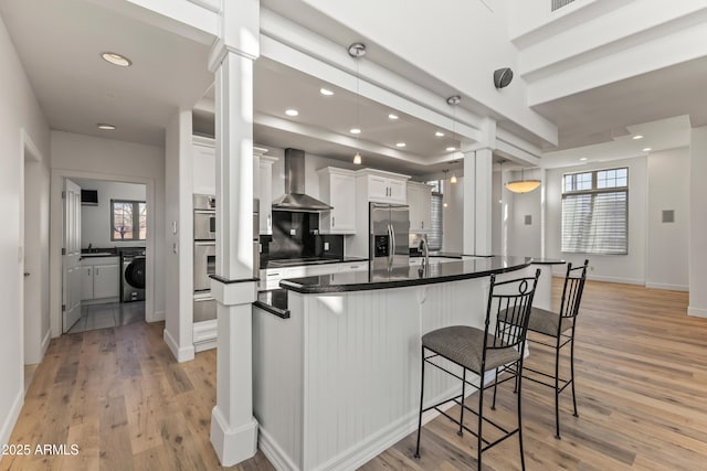 kitchen with a breakfast bar, washer / clothes dryer, white cabinets, wall chimney range hood, and stainless steel fridge with ice dispenser