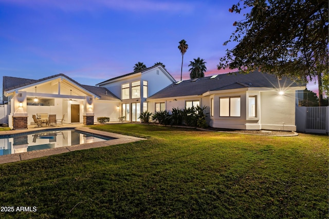 back of house with stucco siding, a lawn, a ceiling fan, a patio area, and an outdoor pool