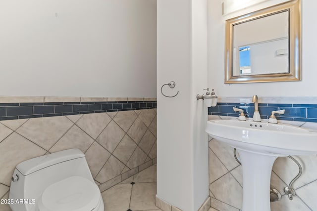 half bath with toilet, a wainscoted wall, a sink, and tile walls