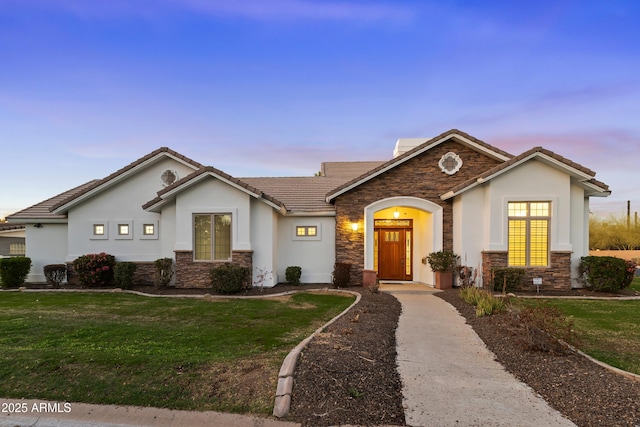 ranch-style home featuring stone siding, a tile roof, a front lawn, and stucco siding