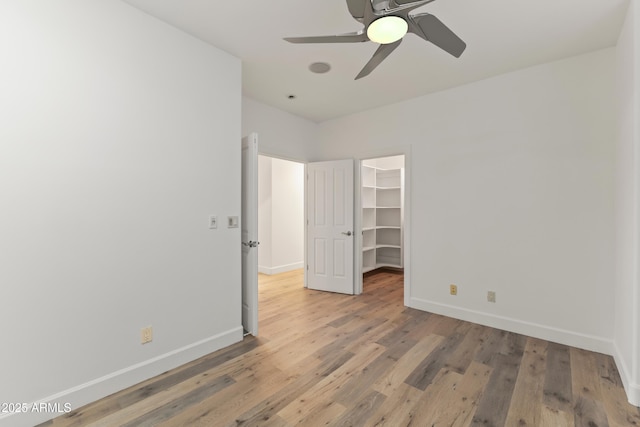 unfurnished bedroom featuring light wood finished floors, baseboards, ceiling fan, a walk in closet, and a closet