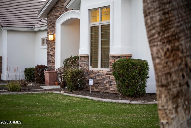 entrance to property featuring stone siding, a yard, and stucco siding