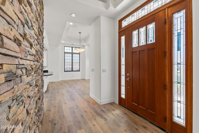 foyer entrance featuring recessed lighting, a tray ceiling, baseboards, and light wood finished floors