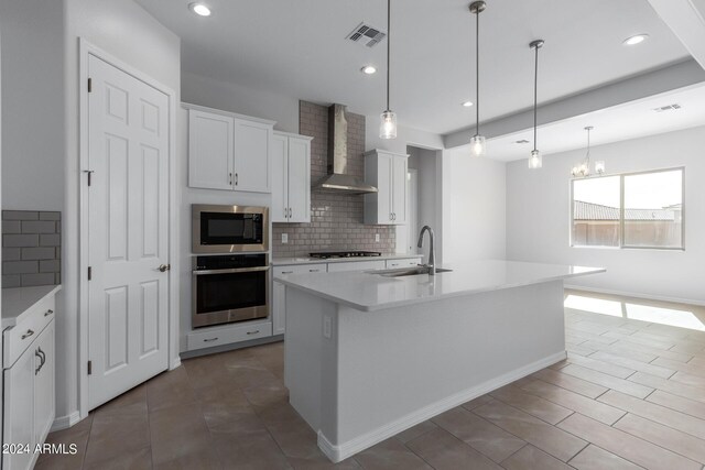 kitchen with decorative backsplash, wall chimney exhaust hood, an island with sink, appliances with stainless steel finishes, and sink