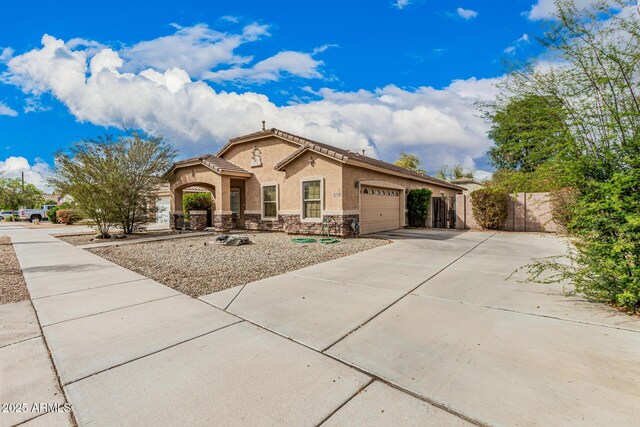 mediterranean / spanish-style house featuring stucco siding, stone siding, fence, concrete driveway, and a garage