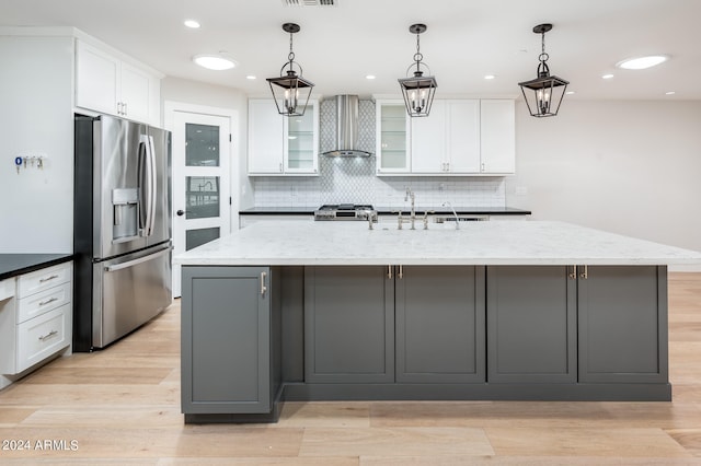 kitchen featuring a kitchen island with sink, wall chimney exhaust hood, white cabinetry, appliances with stainless steel finishes, and dark stone countertops