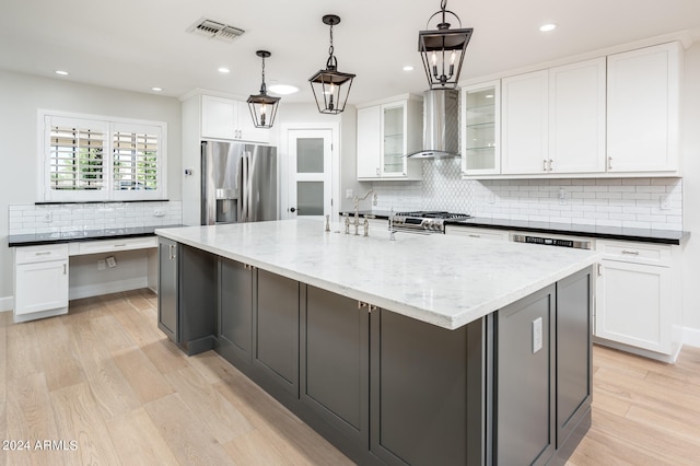 kitchen with appliances with stainless steel finishes, a large island with sink, wall chimney exhaust hood, and white cabinetry