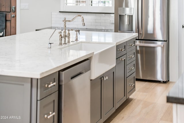 kitchen with appliances with stainless steel finishes, backsplash, light stone countertops, gray cabinets, and light hardwood / wood-style flooring