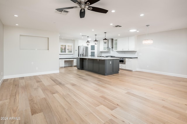 kitchen with pendant lighting, white cabinets, a center island with sink, wall chimney range hood, and appliances with stainless steel finishes