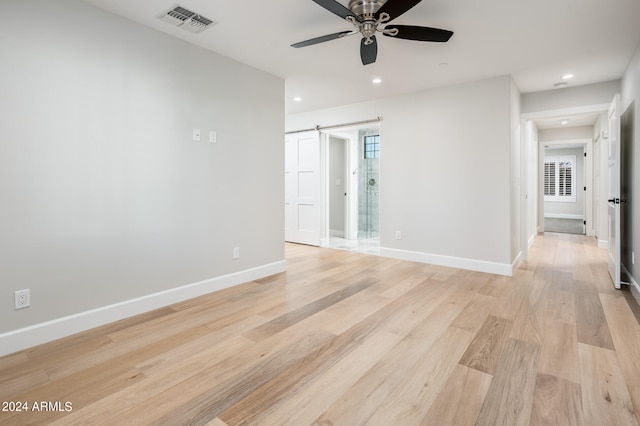 spare room with a barn door, light hardwood / wood-style floors, and ceiling fan