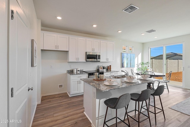 18052 W Sand Hills Rd, Surprise, AZ 85387 - kitchen with white cabinets, wood finished floors, visible vents, and stainless steel microwave