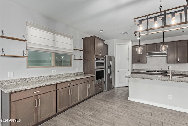 kitchen featuring sink, light stone counters, dark brown cabinets, stainless steel appliances, and decorative light fixtures